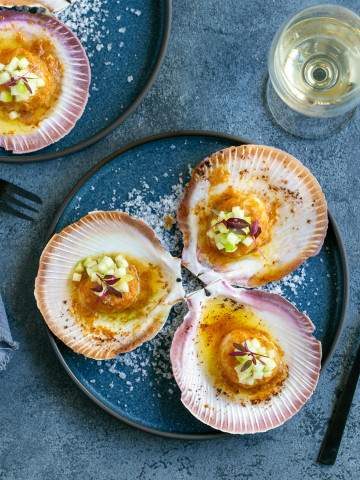 Three Oven Baked Scallops with Miso and Ginger Butter in a plate with a glass of wine on the side