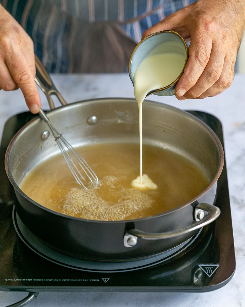 Adding cream to reduced chicken stock in pan 