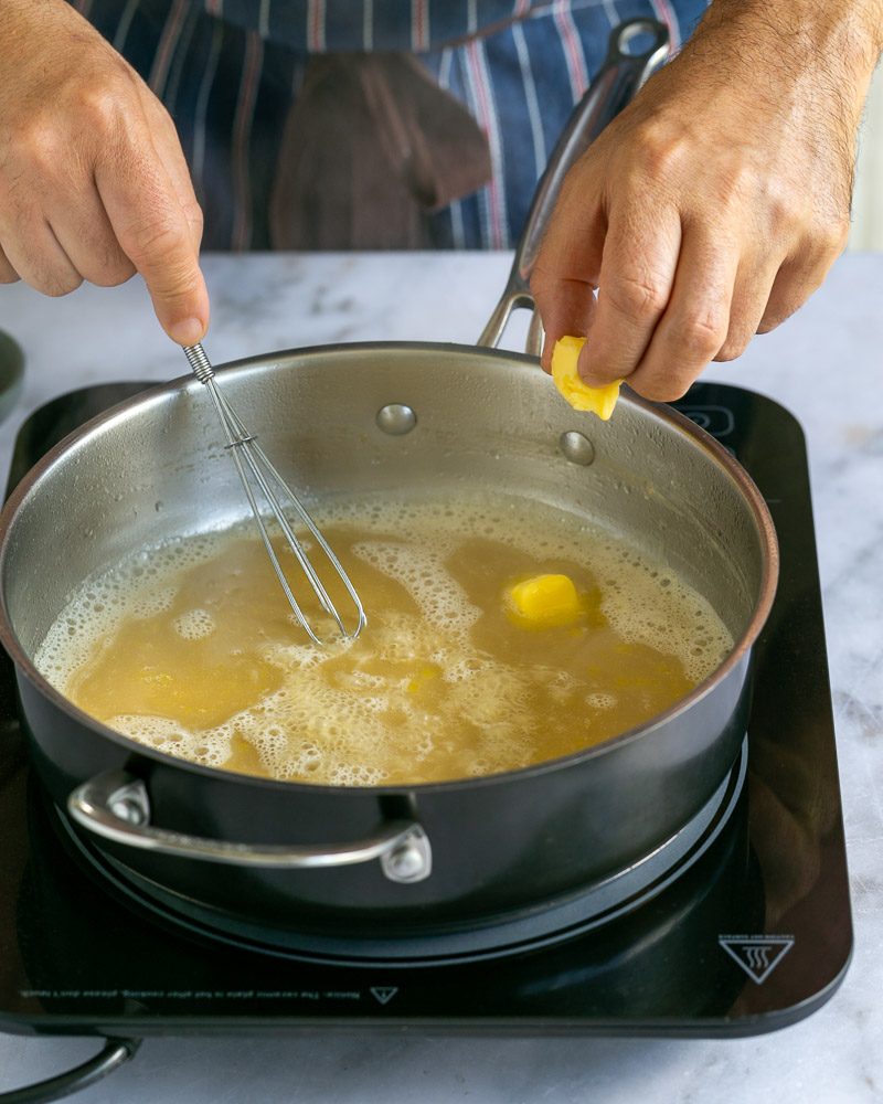 Adding butter to reduced chicken stock in pan 