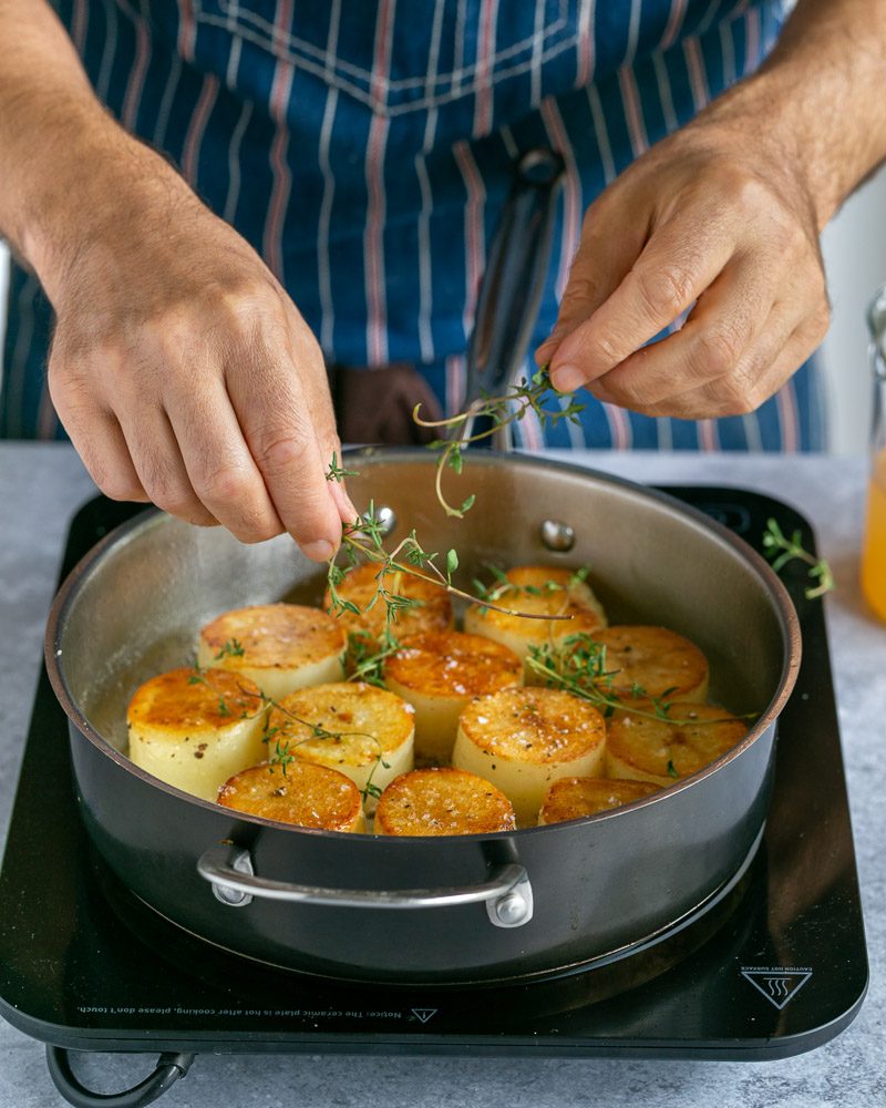 Adding thyme sprigs to the potatoes in the pan