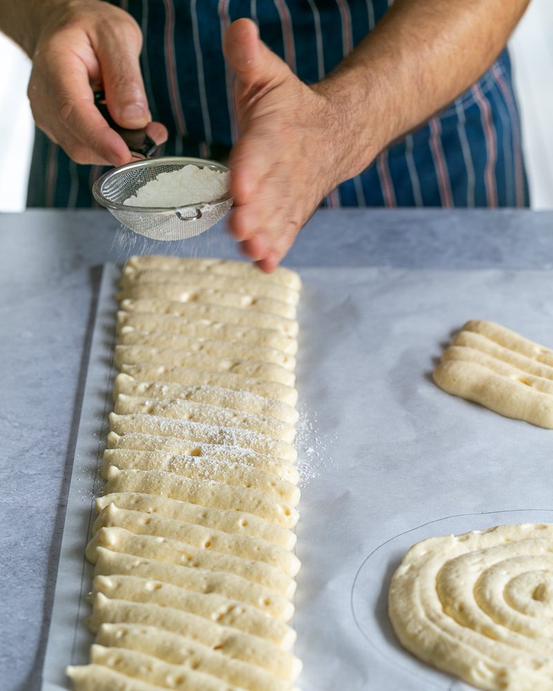 Dusting piped sponge cake and ladyfingers with icing sugar