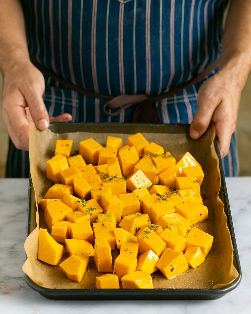 Pumpkin cubes tossed in olive oil and herbs on a baking tray