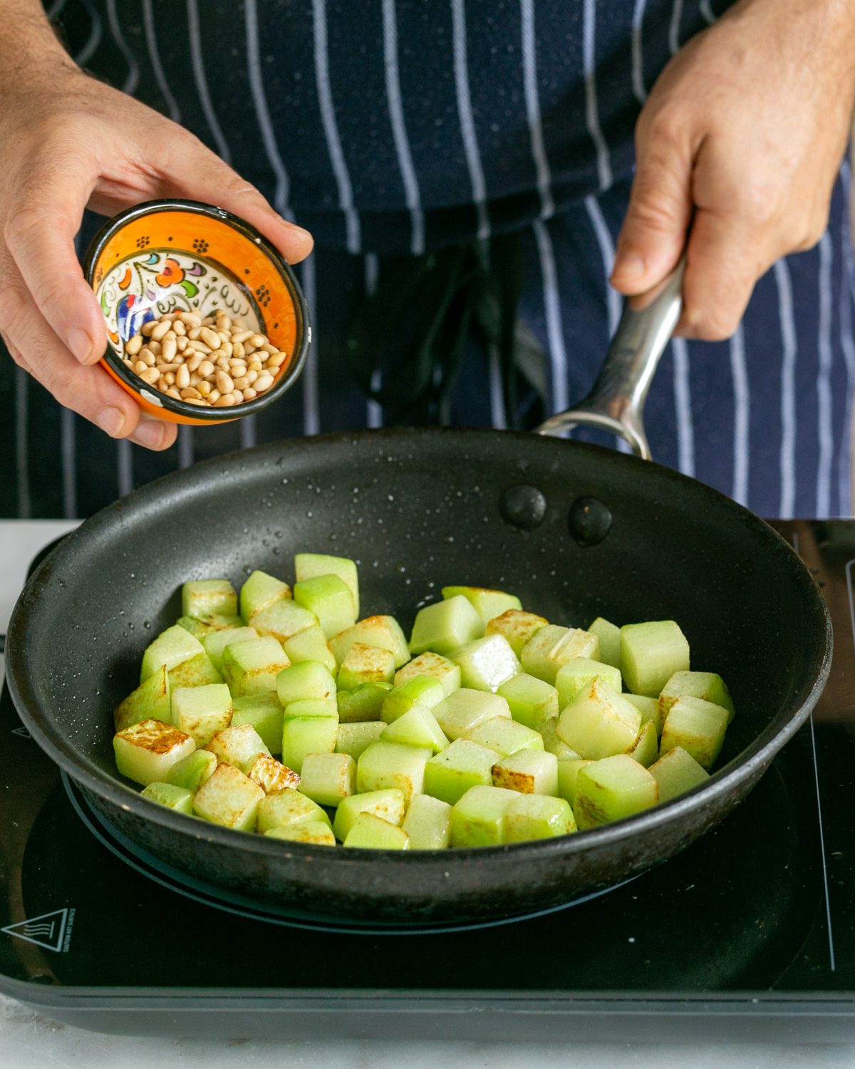 Adding pine seeds to roasted chokos in pan