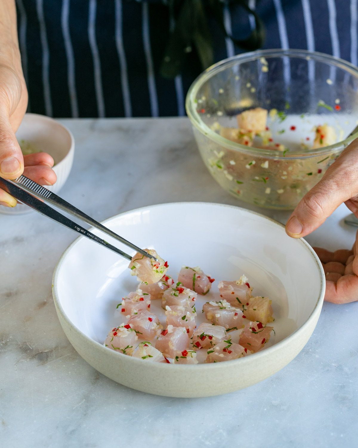 Placing the marinated hamachi cubes in a bowl with tweezers