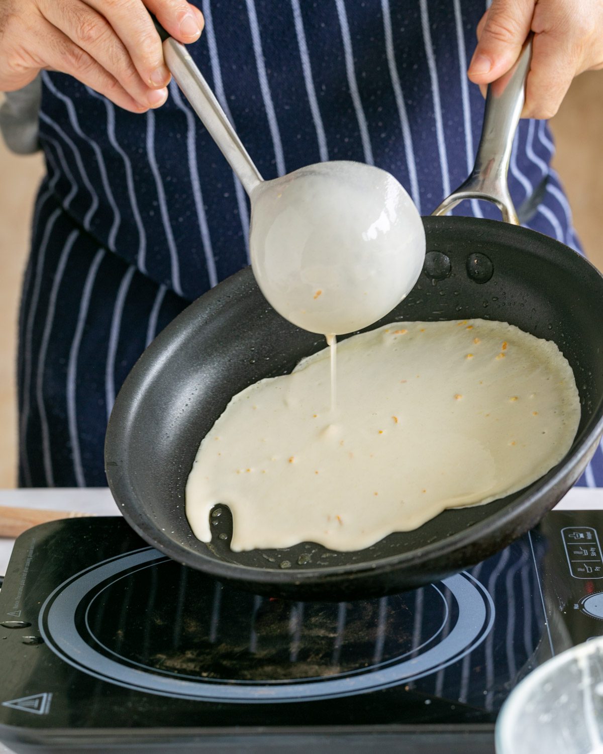 Pouring crepe batter with a ladle to the hot pan