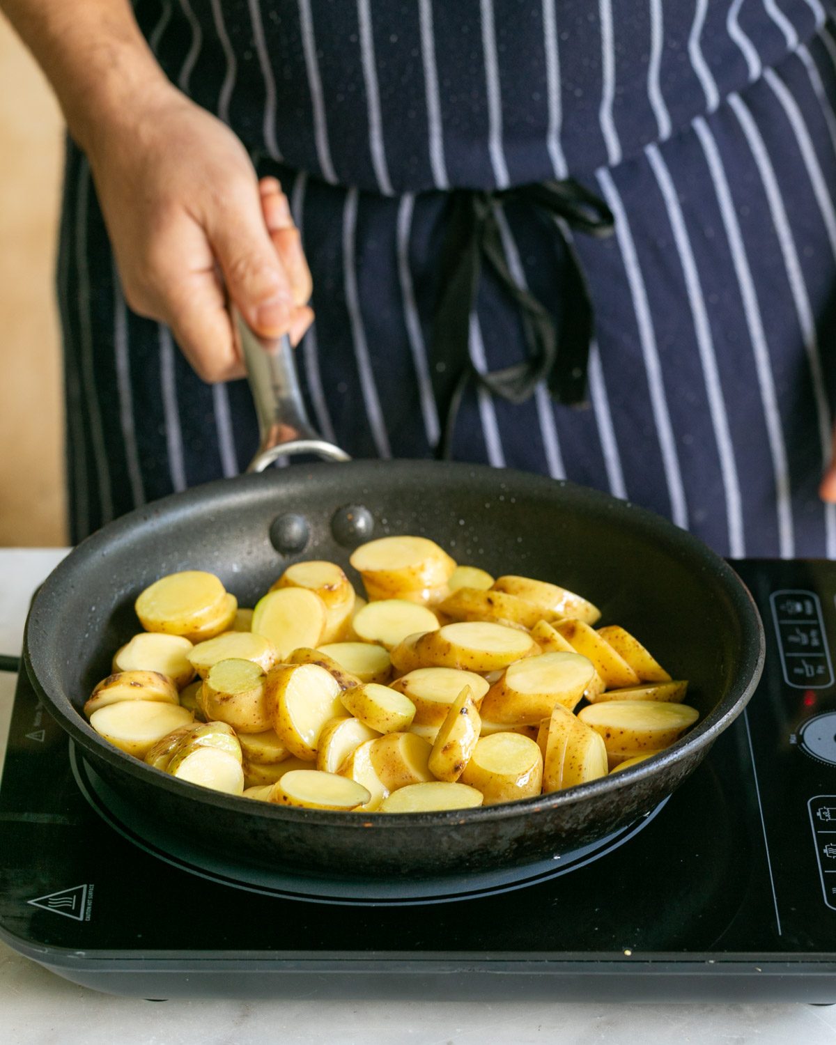 Roasting cut kipfler potatoes in a pan